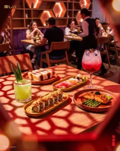 Mesa de Tanoshii Salitre con rollos de sushi, nigiris, salmón y cocteles, con el comedor del restaurante al fondo