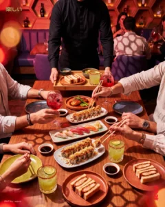 Mesero sirviendo una bandeja mientras un grupo comparte rollos de sushi, nigiris y cocteles en Tanoshii Salitre